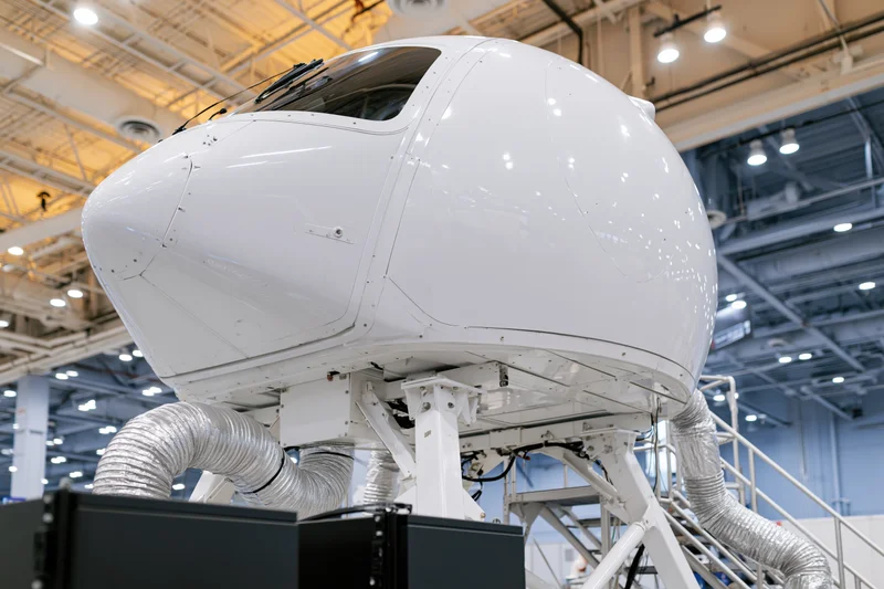 White dome-shaped flight simulator pod mounted on metal support frame inside industrial facility