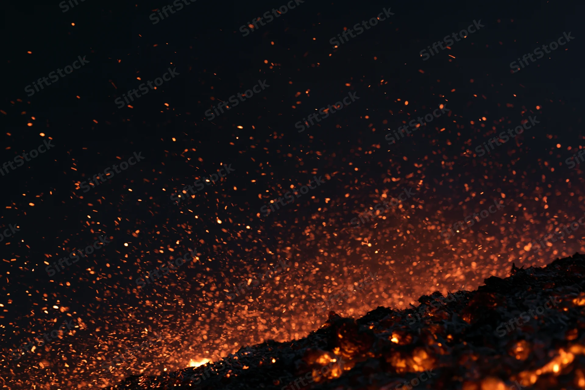 Glowing embers and sparks rising from burning material at night