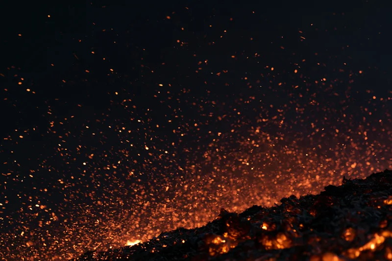 Glowing embers and sparks rising from burning material at night