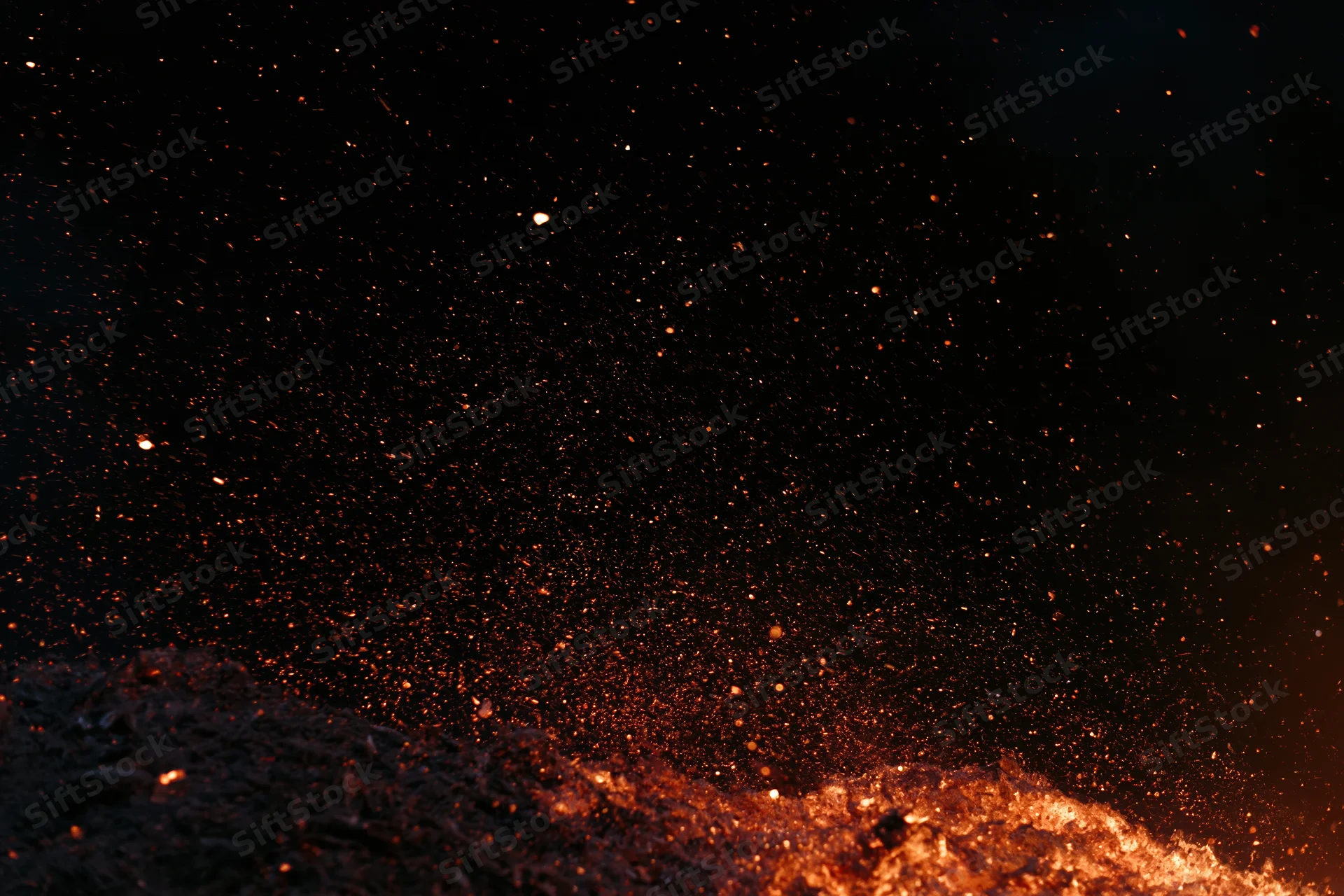 Glowing embers and sparks rising from burning material in darkness
