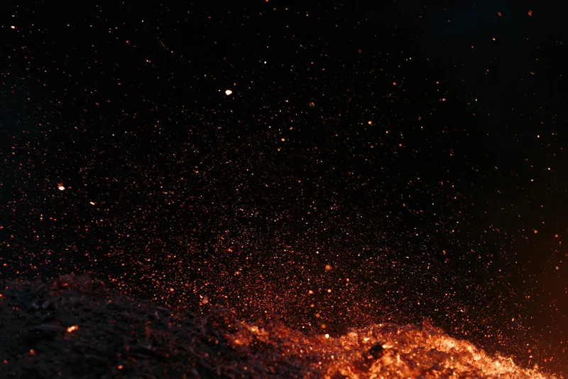 Glowing embers and sparks rising from burning material in darkness
