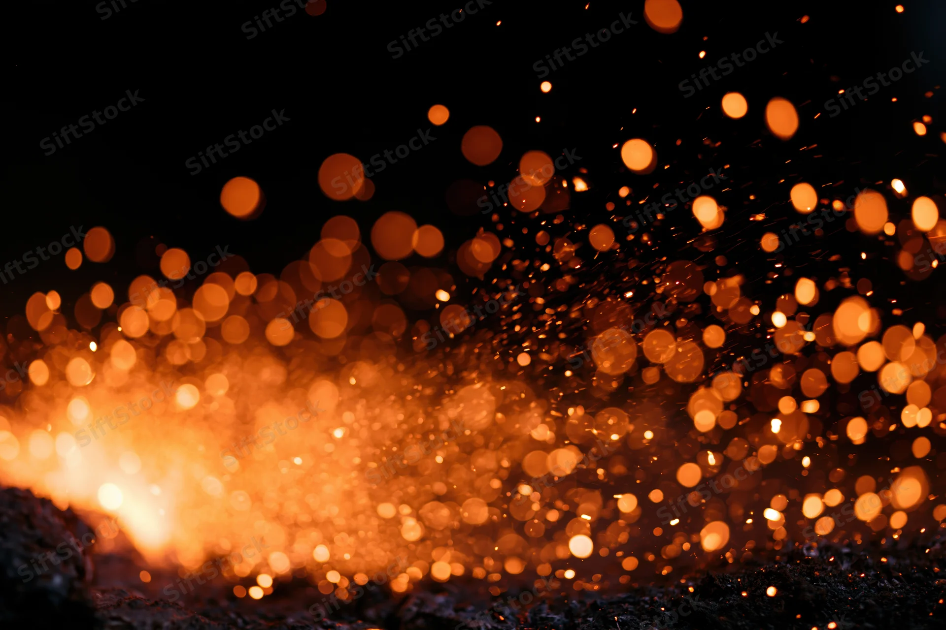 Glowing orange sparks flying upward from a fire source against a dark background