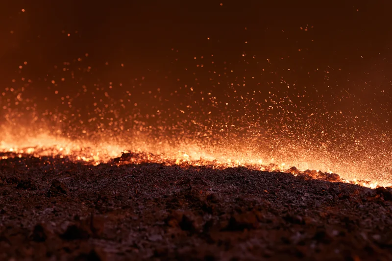 Fire burning across dark scorched earth at night