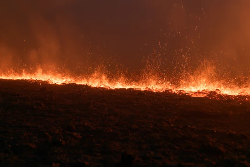 Low-angle view of fire burning across dark scorched earth at night