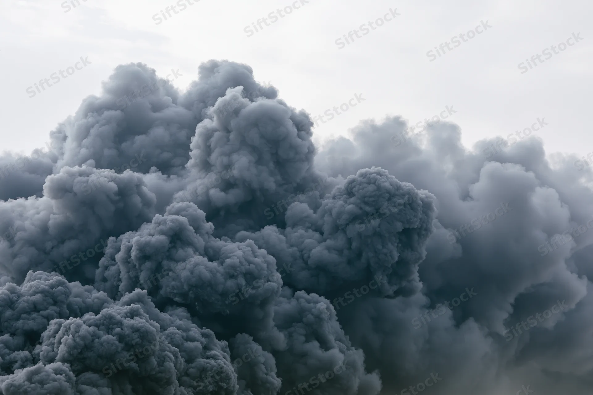 Massive billowing column of dark grey smoke rising into the overcast sky
