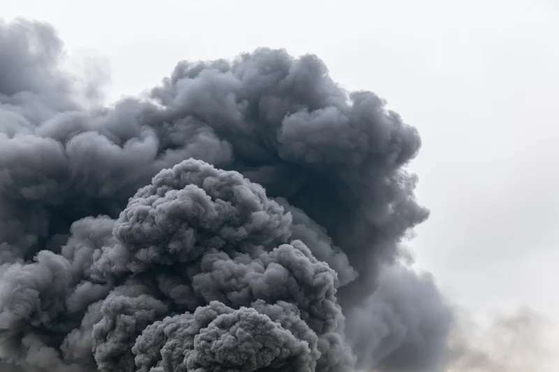 Massive billowing column of dark grey smoke rising into overcast sky