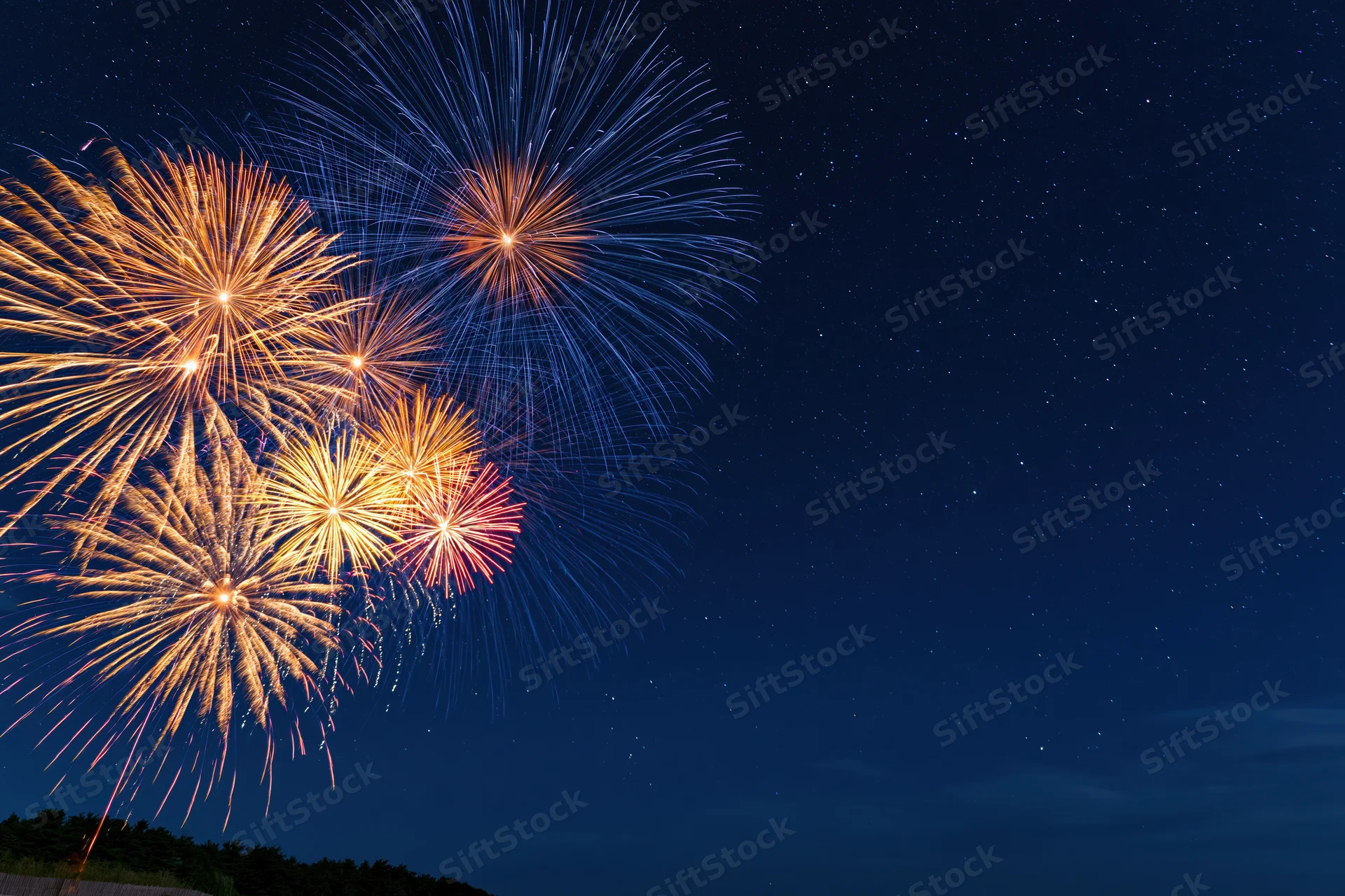 Fireworks bursting in the night sky over a dark landscape with stars visible in the background
