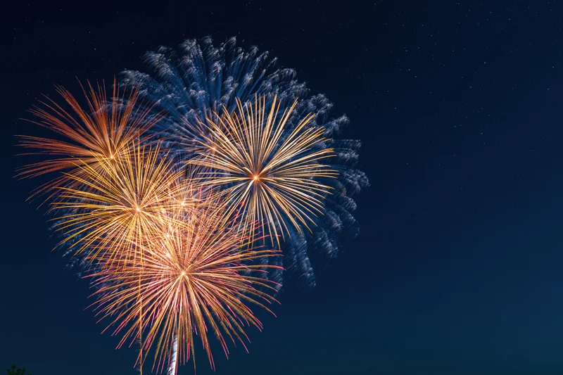 Fireworks bursting in the night sky with colorful trails and smoke against a dark starry background