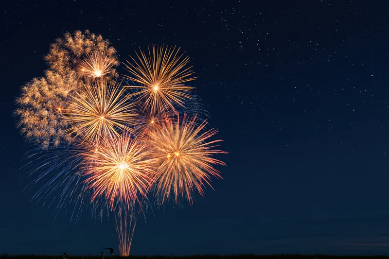 Fireworks bursting in the night sky over a dark landscape with stars visible