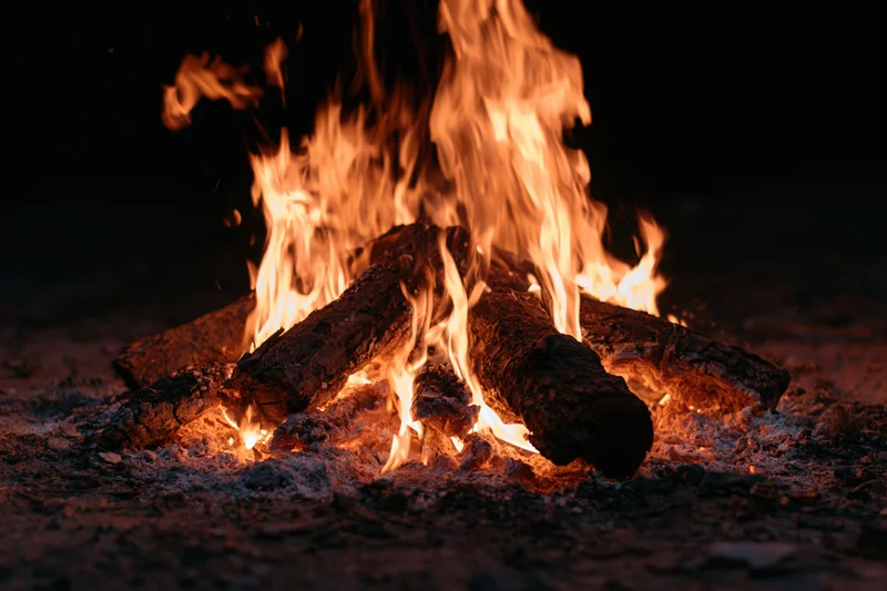 Campfire burning with flames rising from stacked logs on dark ground at night