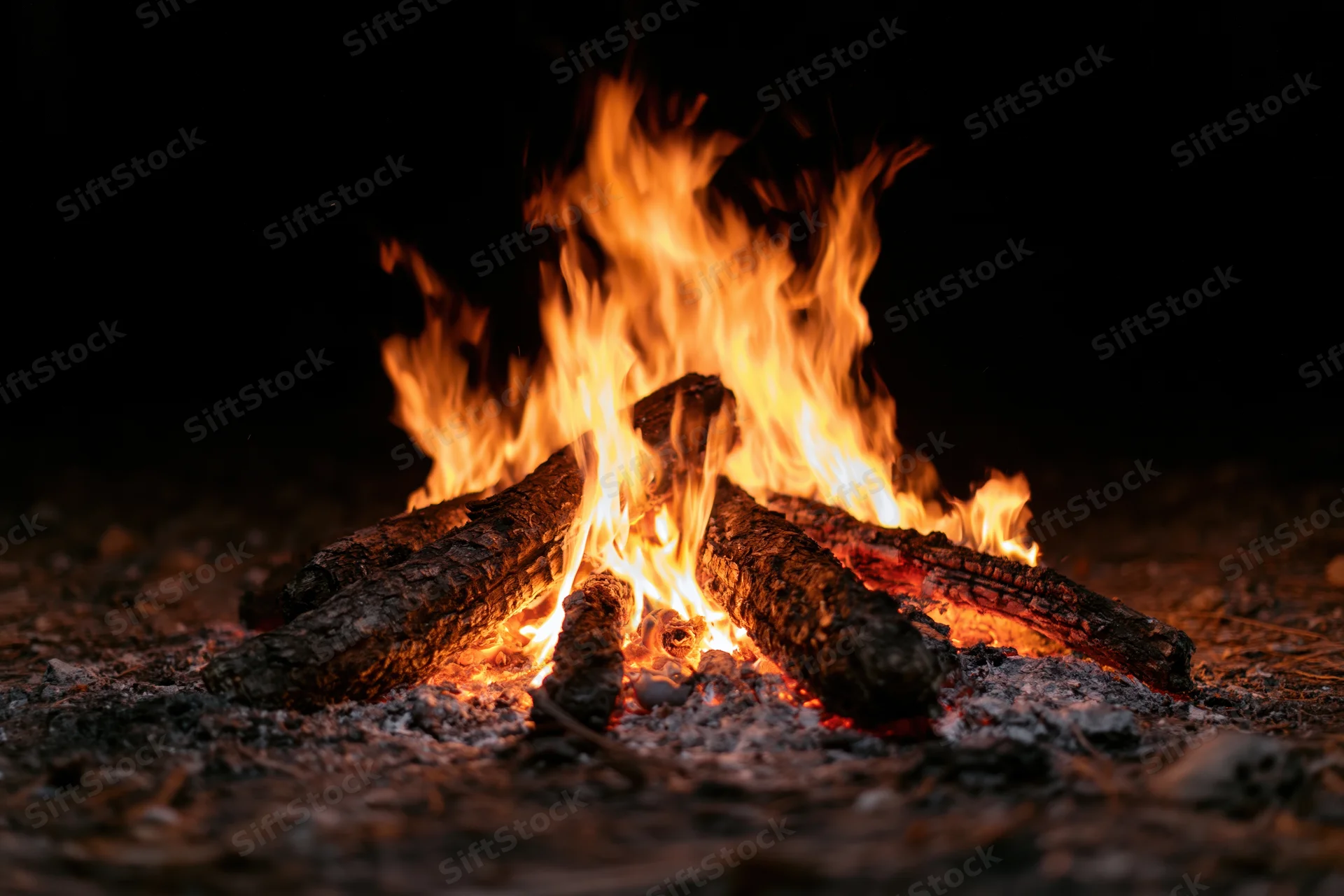 Campfire burning with flames rising from stacked logs on dark ground at night