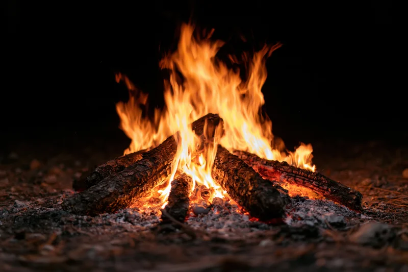 Campfire burning with flames rising from stacked logs on dark ground at night