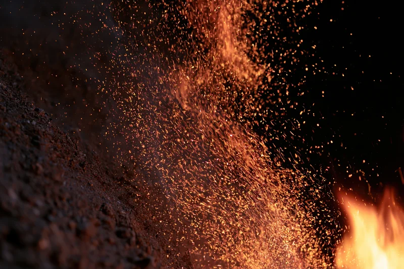 Sparks flying upward from a burning fire against a dark background