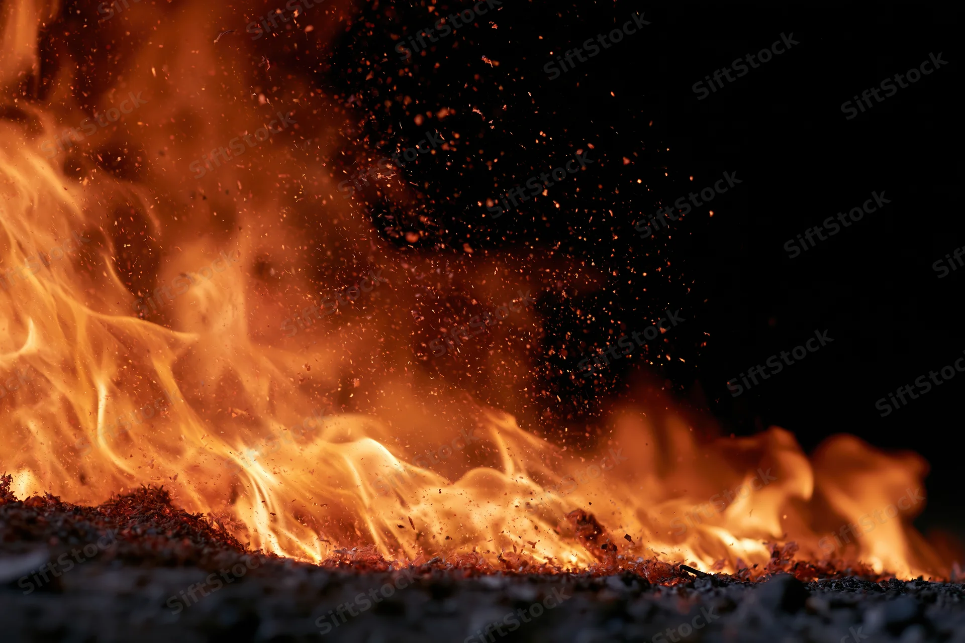 Flames burning intensely against a black background with flying sparks and glowing embers