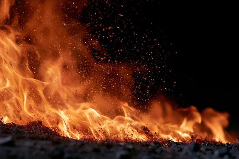 Flames burning intensely against a black background with flying sparks and glowing embers