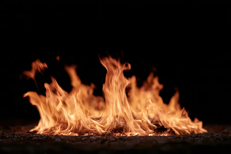 Flames burning low on a dark ground surface against a black background