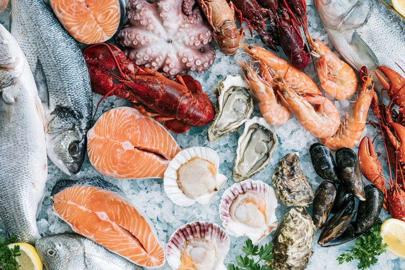 Overhead flat-lay of fresh seafood including salmon, lobster, shrimp, oysters and scallops arranged on ice at a market display