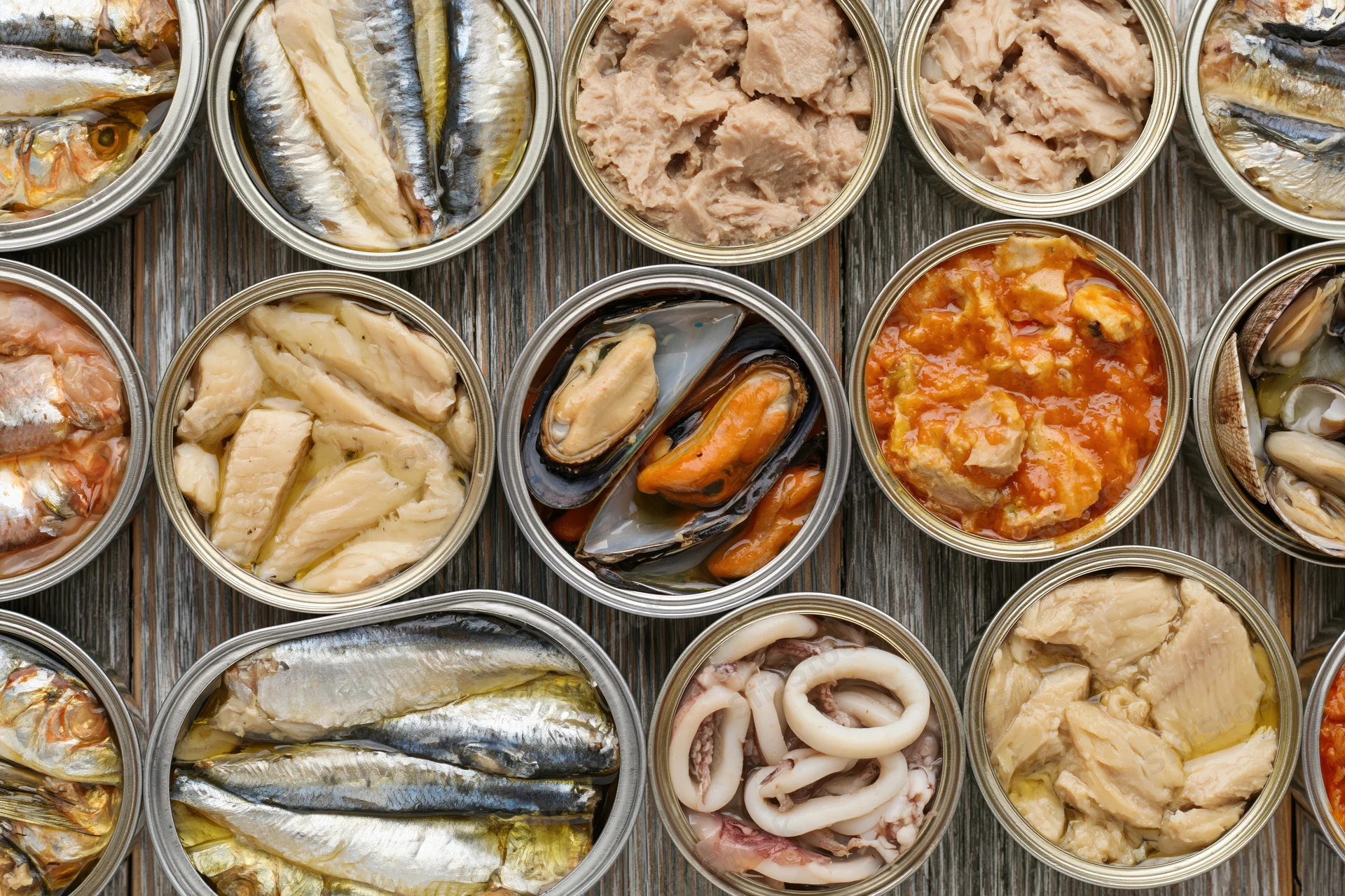 Overhead flat lay of open tin cans filled with various canned seafood arranged on a wooden surface