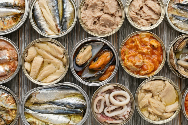 Overhead flat lay of open tin cans filled with various canned seafood arranged on a wooden surface