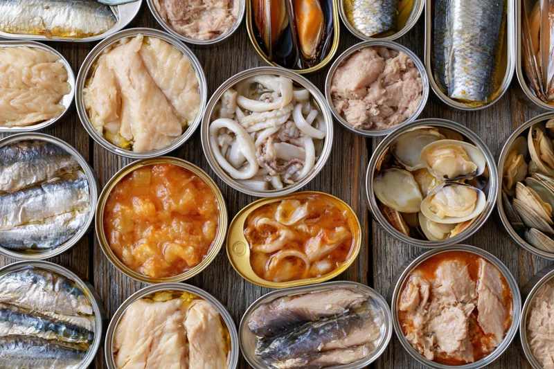 Overhead flat lay of open tin cans filled with various canned seafood arranged on wooden surface