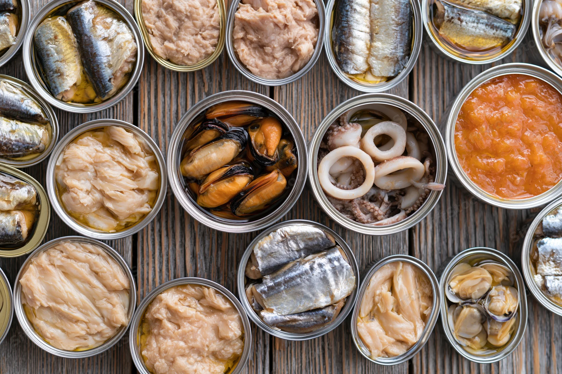 Overhead flat lay of open tin cans filled with various canned seafood arranged on a wooden table