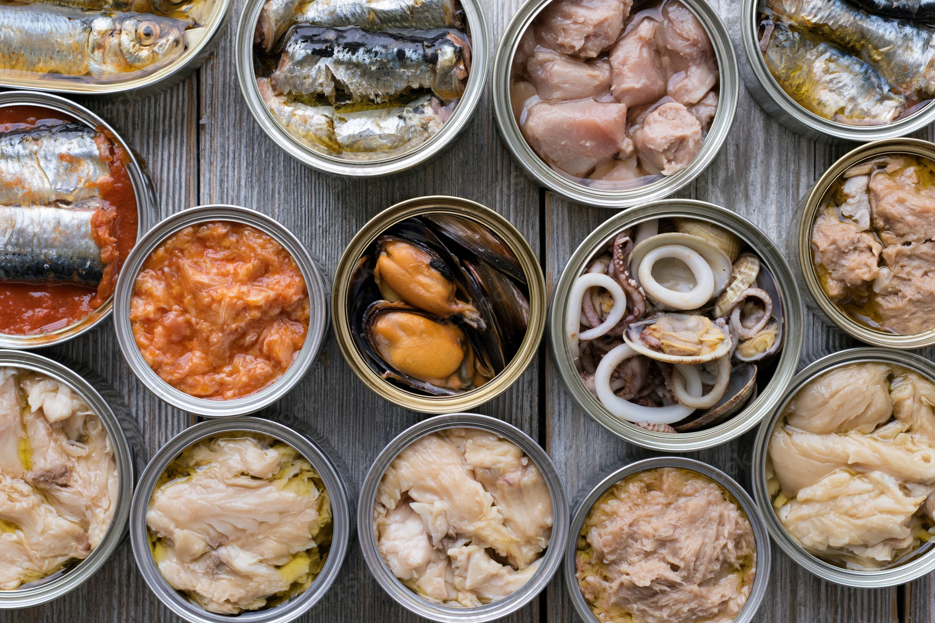 Overhead flat lay of open tin cans filled with various canned seafood arranged on a wooden surface