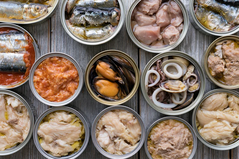 Overhead flat lay of open tin cans filled with various canned seafood arranged on a wooden surface
