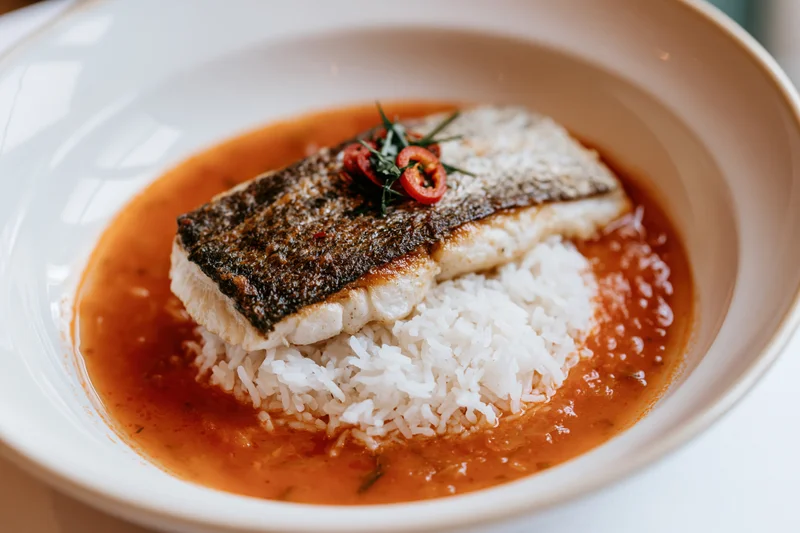 Pan-seared fish fillet with crispy skin on rice in tomato sauce in a white bowl