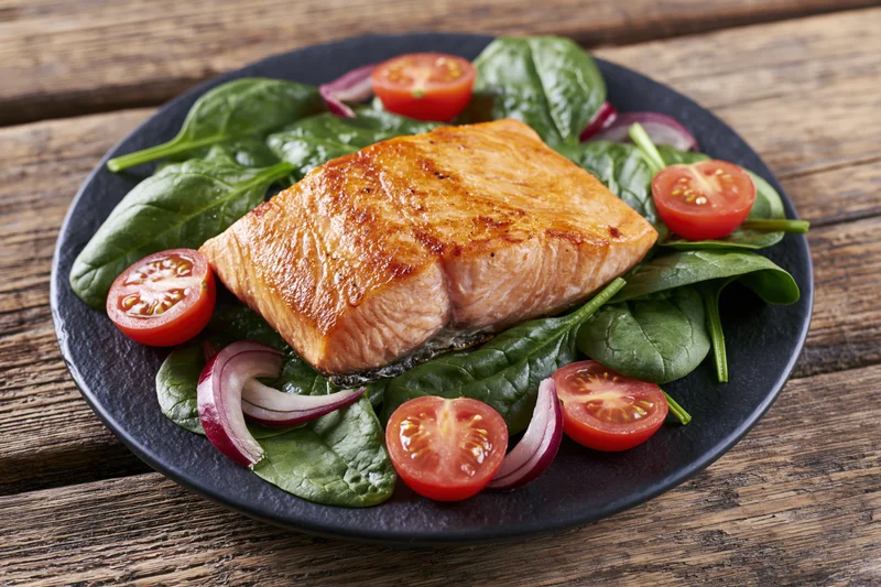 Pan-seared salmon fillet with spinach and cherry tomatoes on a black plate on wooden table