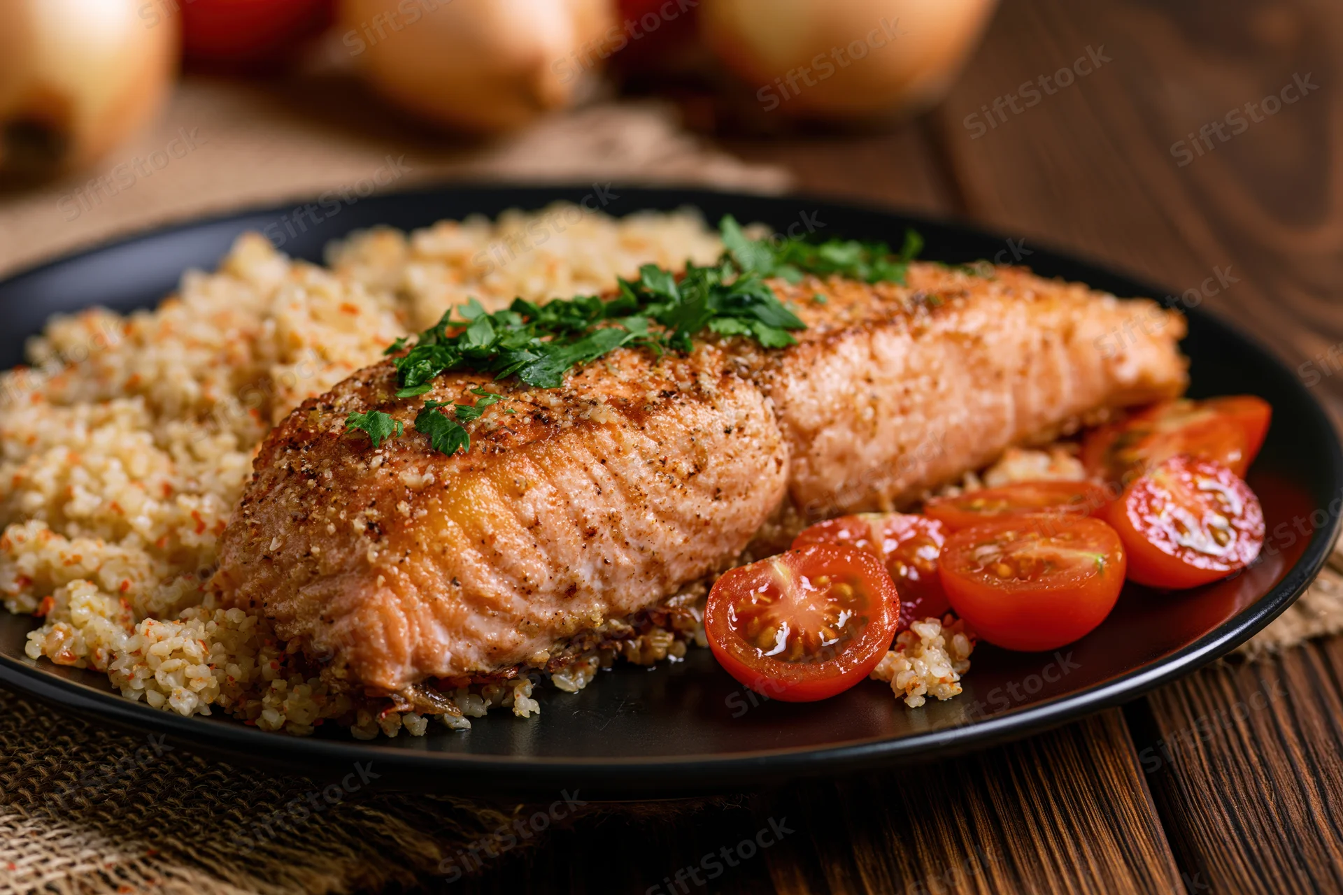 Pan-seared salmon fillet with golden-brown crust served on black plate with bulgur and cherry tomatoes