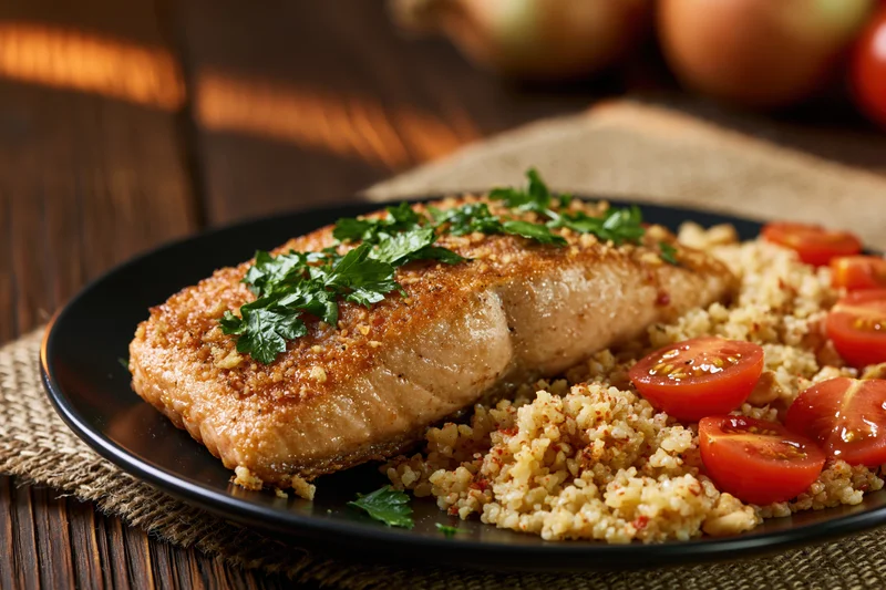 Pan-seared salmon fillet with golden-brown crust served on black plate with quinoa and cherry tomatoes