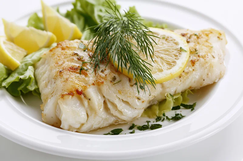 Pan-seared white fish fillet garnished with lemon and dill on a white plate