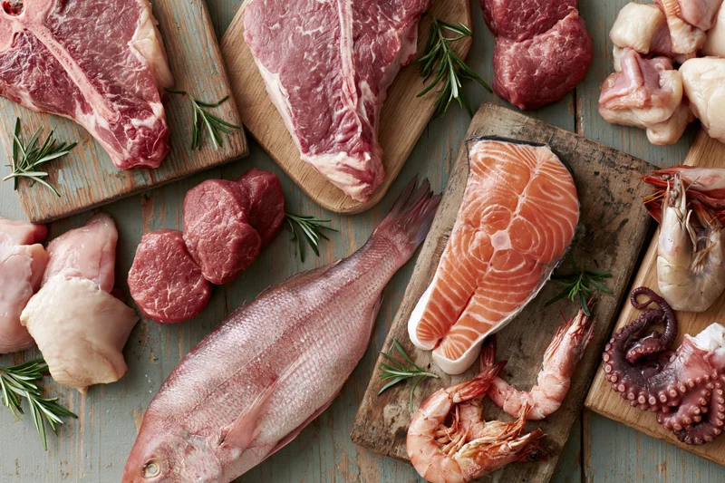 Raw meat seafood and poultry arranged on wooden cutting boards with rosemary sprigs