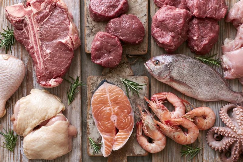 Raw meat seafood and poultry arranged on wooden cutting boards with rosemary sprigs