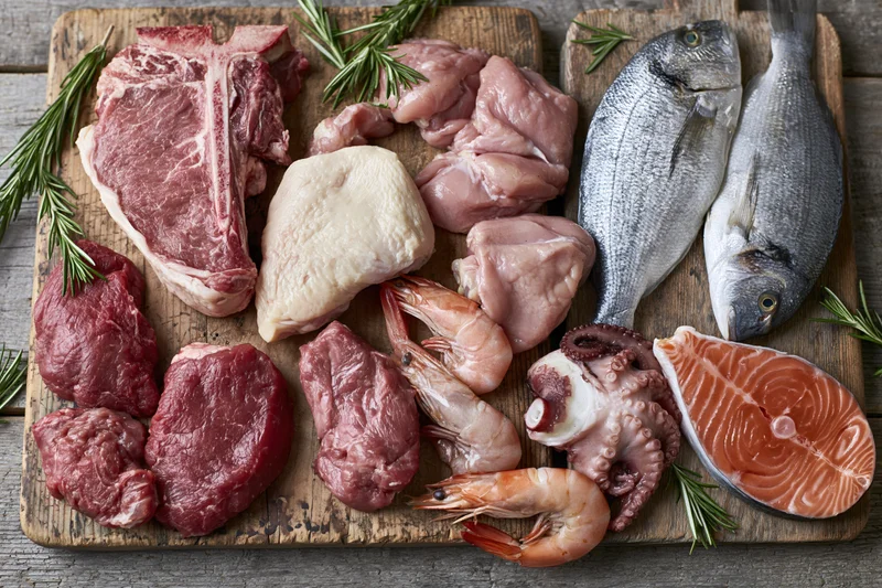 Raw meat seafood and poultry arranged on a worn wooden cutting board