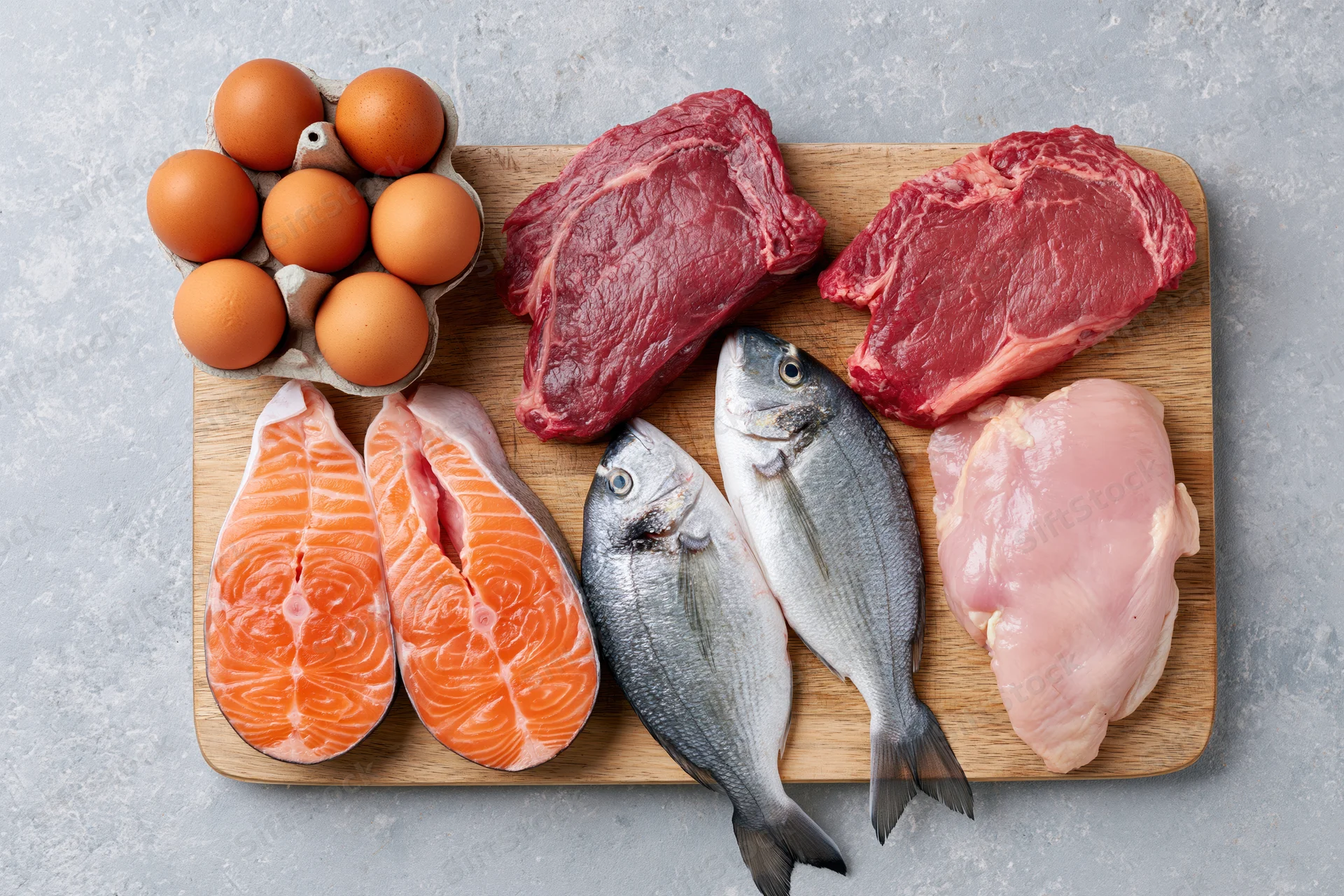 Raw protein foods arranged flat lay on a light gray stone surface