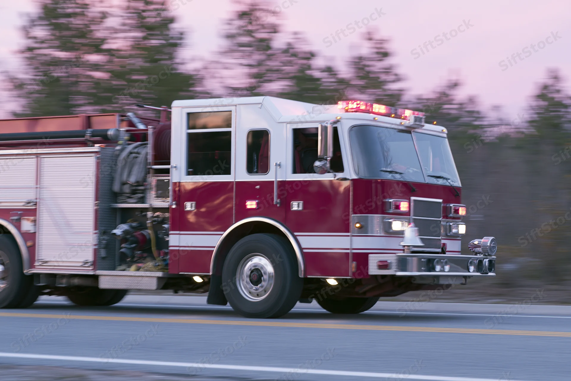 Red and white fire truck speeding down suburban road with emergency lights on