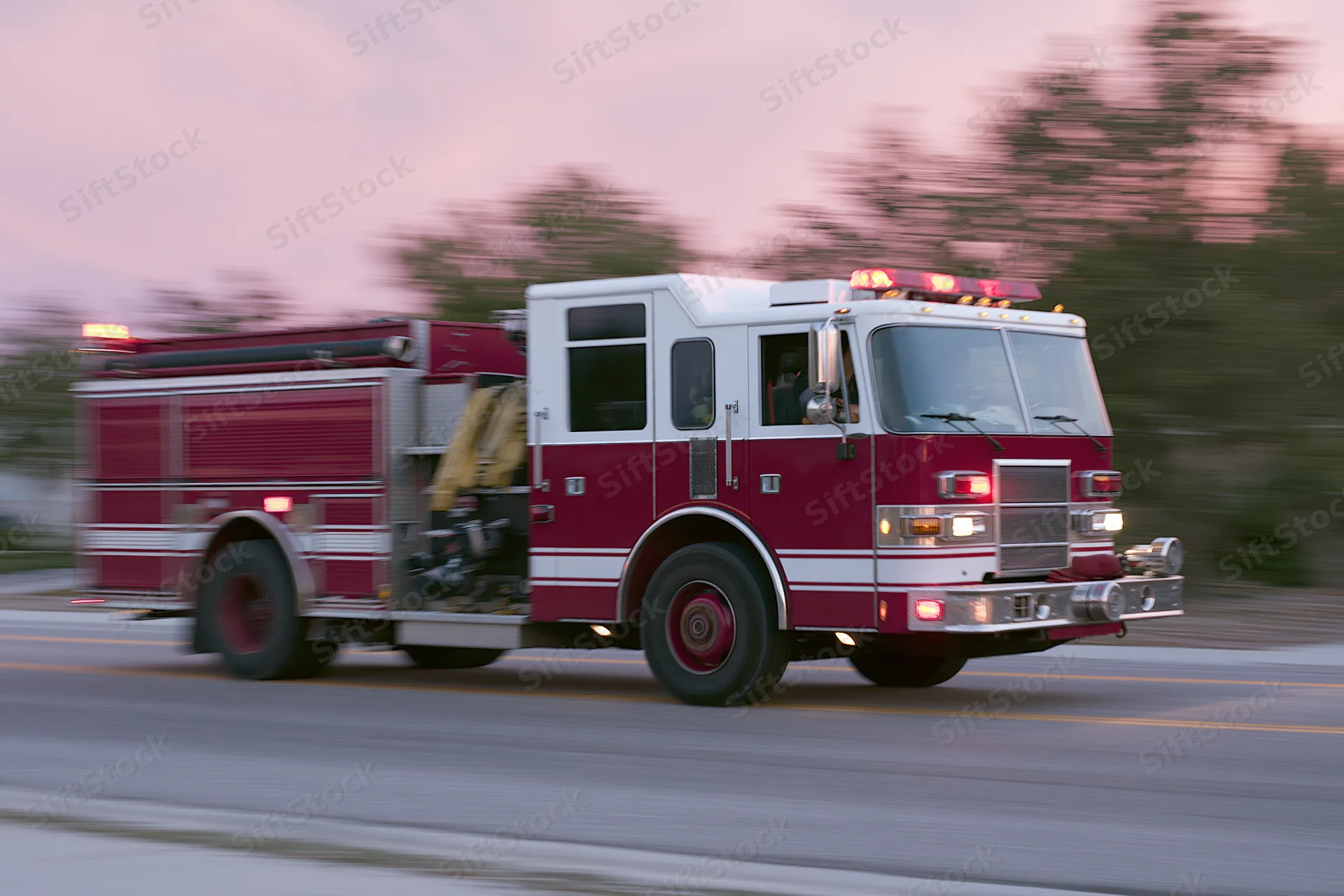 Red and white fire truck speeding down suburban road with flashing lights and motion blur