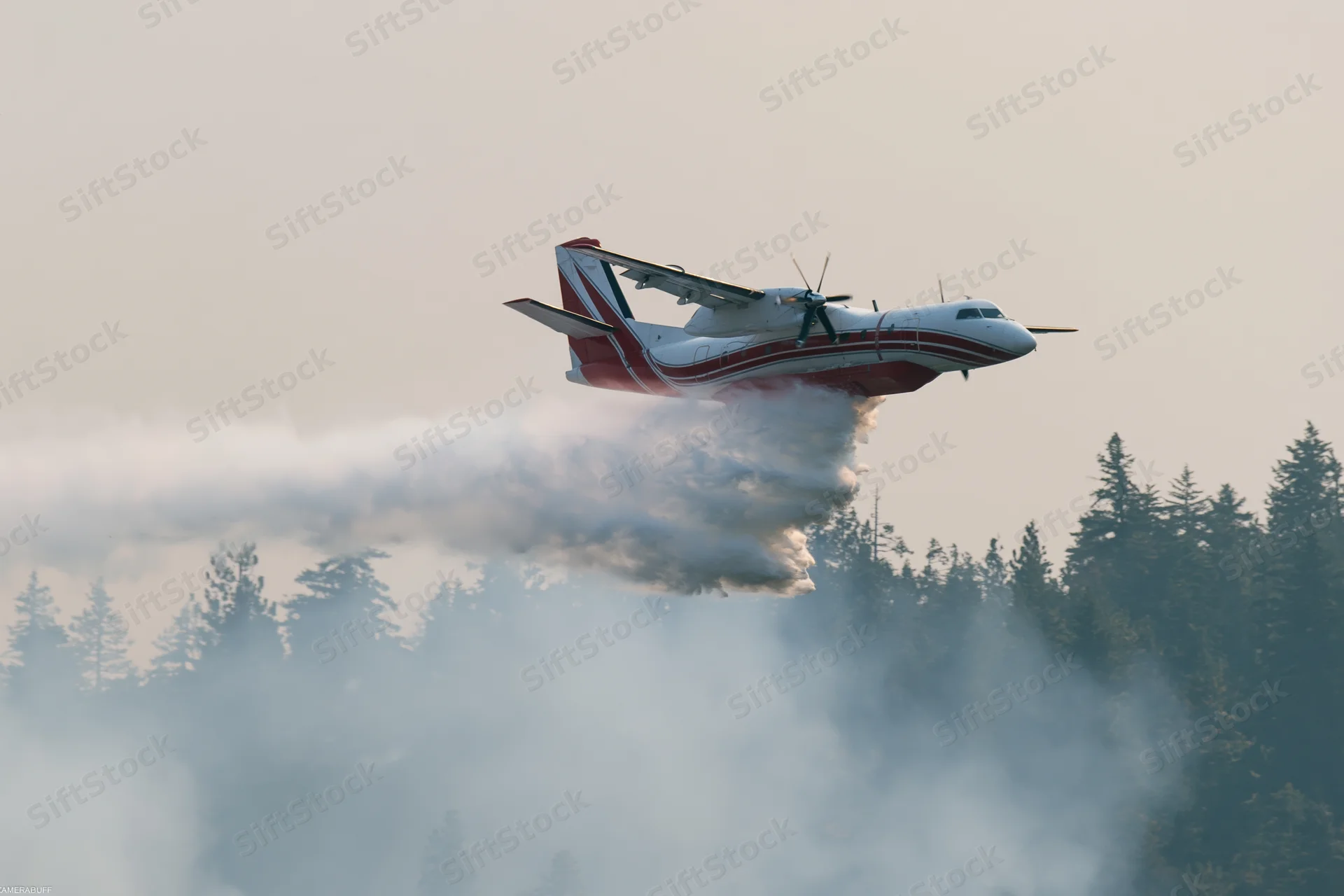 Red and white turboprop airtanker spraying retardant over forest during low flight