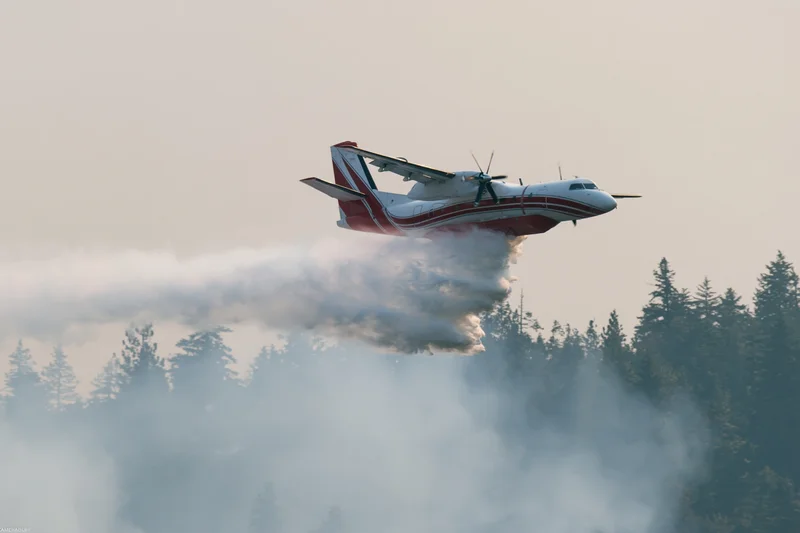 Red and white turboprop airtanker spraying retardant over forest during low flight