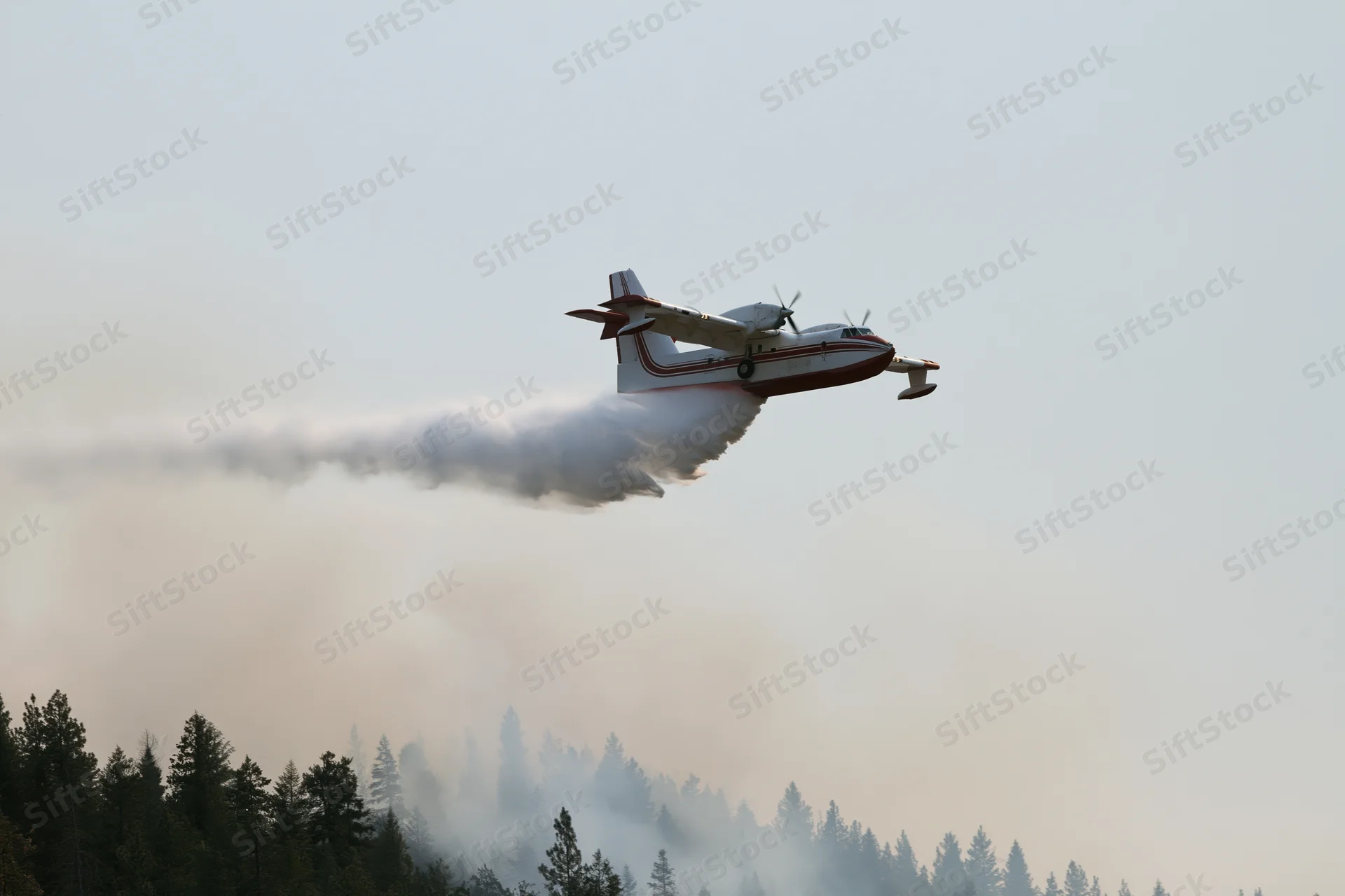 Red and white turboprop airtanker releasing water over forested area during wildfire suppression operation