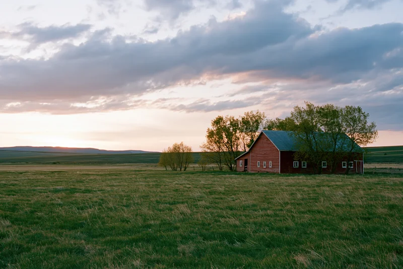 Red barn in a wide green pasture at golden hour