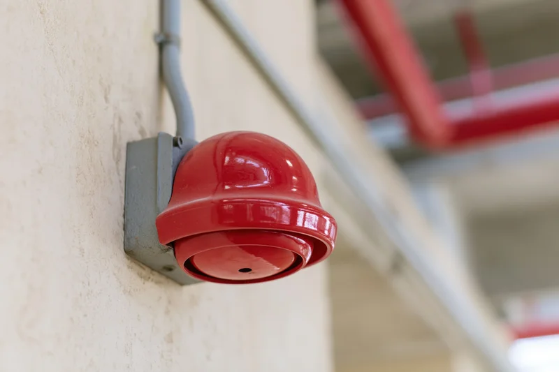 Red dome fire alarm bell mounted on a pale concrete wall in an industrial building interior