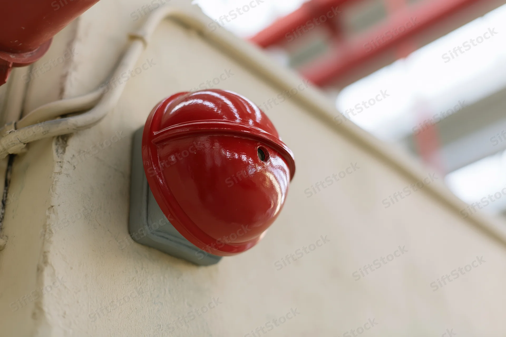 Red dome fire alarm bell mounted on a pale concrete wall in an industrial building interior