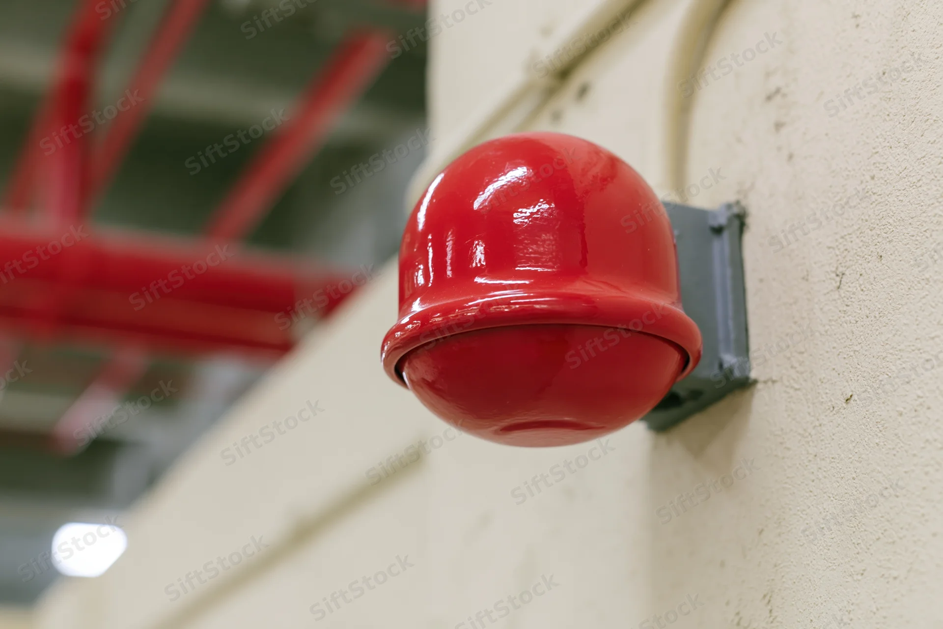 Red dome fire alarm bell mounted on a concrete wall in an industrial building interior
