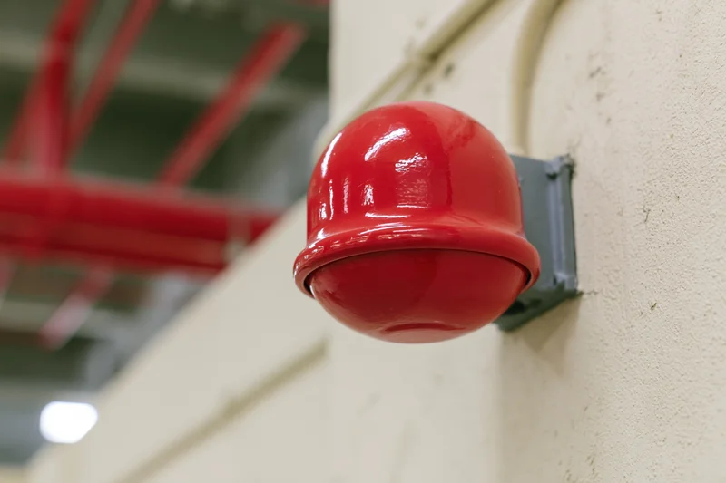 Red dome fire alarm bell mounted on a concrete wall in an industrial building interior