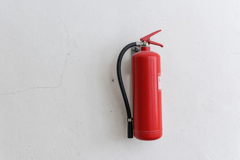 Red dry chemical powder fire extinguisher mounted on a white wall in an interior space