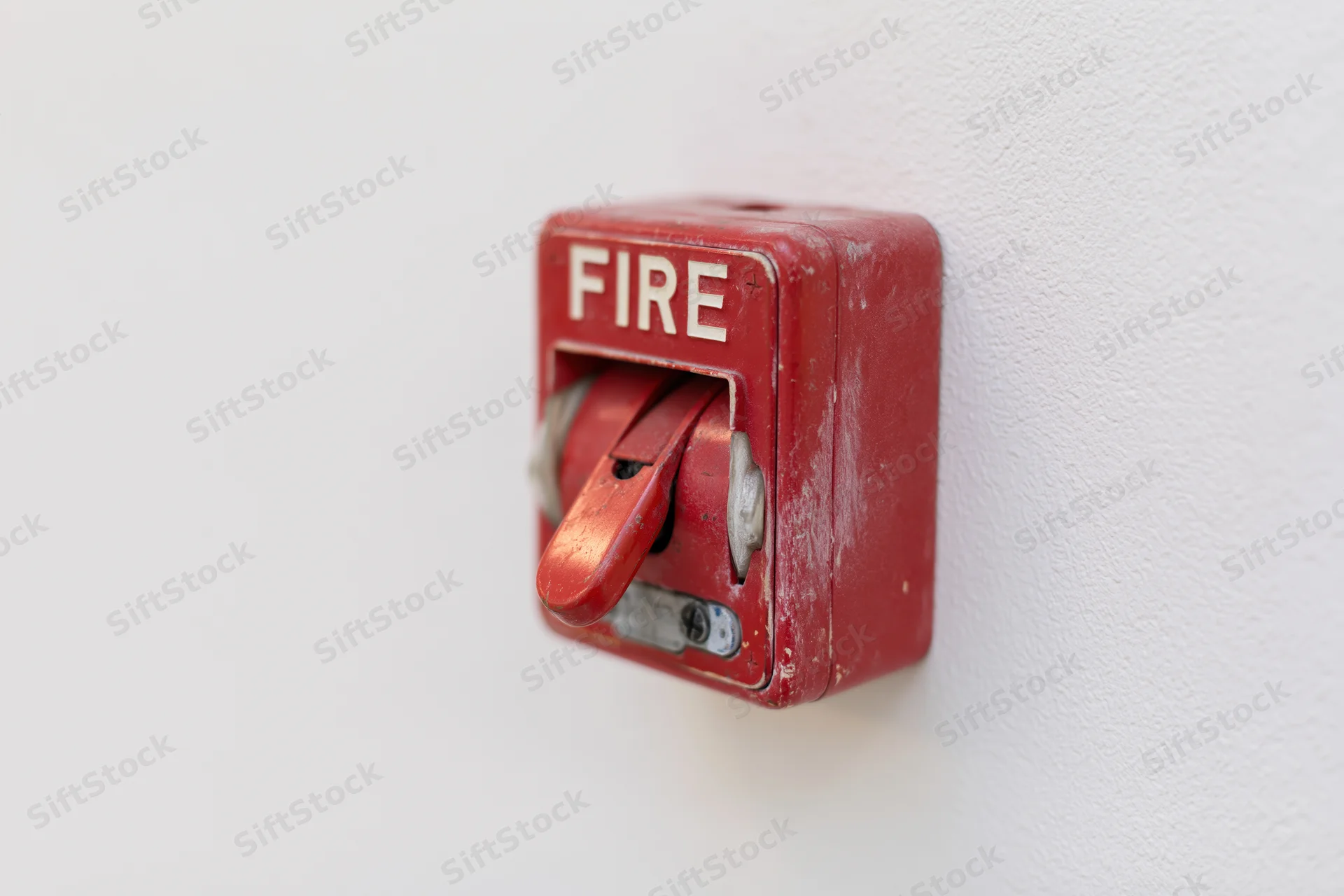Red fire alarm pull station mounted on a white textured wall