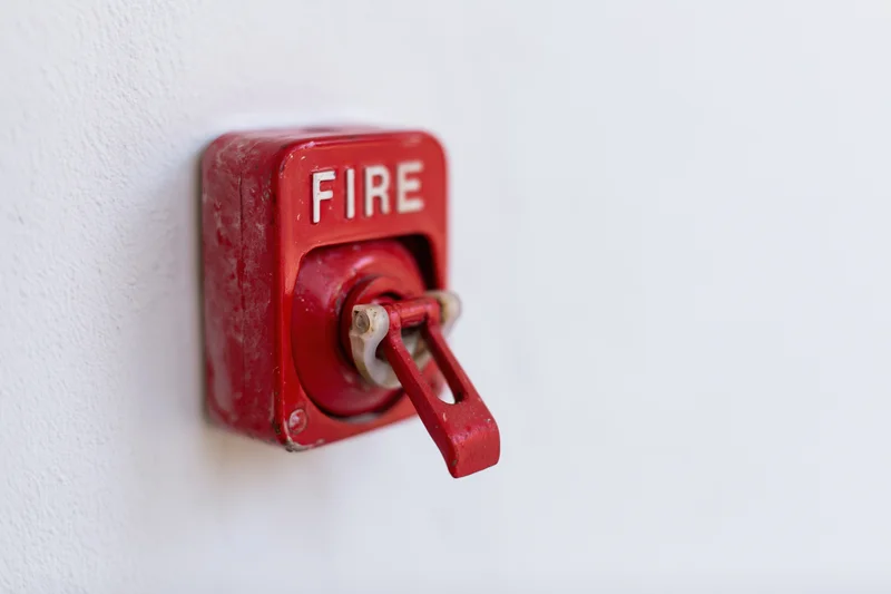 Red fire alarm pull station mounted on a white textured wall