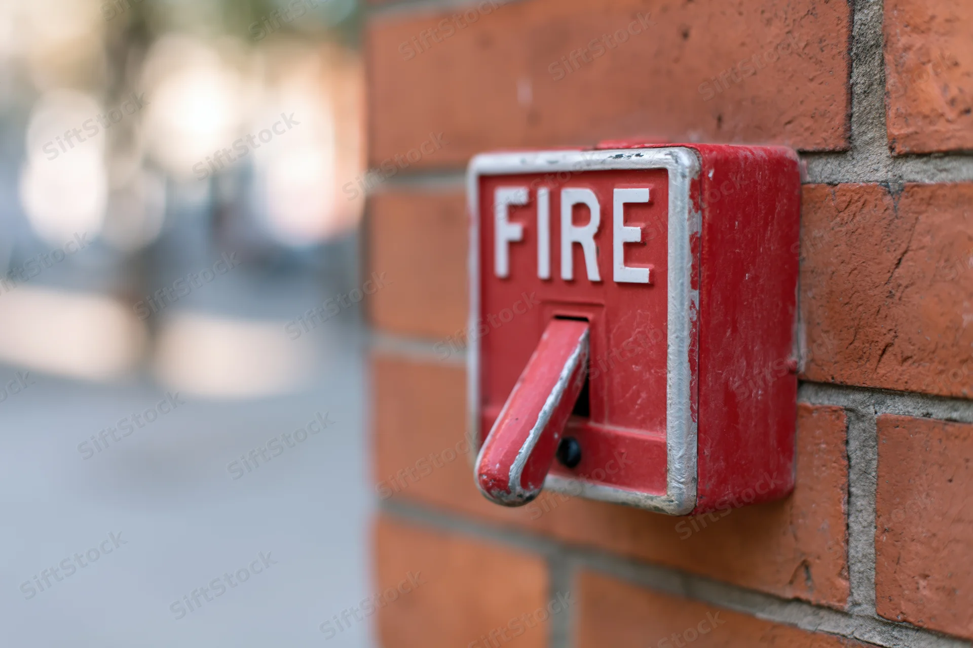 Red fire alarm pull station mounted on a brick wall outdoors